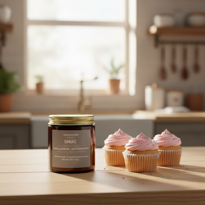 ECOWORTHPRO SNUG vanilla buttercream candle surrounded by pink frosted cupcakes with sprinkles on a bright kitchen counter, artisan dessert scented mini candle
